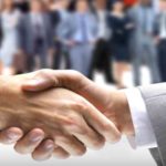 大勢のスーツ姿の労働者を背景に握手をしている2人