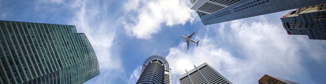 立ち並ぶオフィスビルを見上げると雲の合間に飛行機が飛んでいる