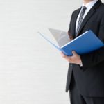 青色のファイルを手に解説するスーツ姿の専門家