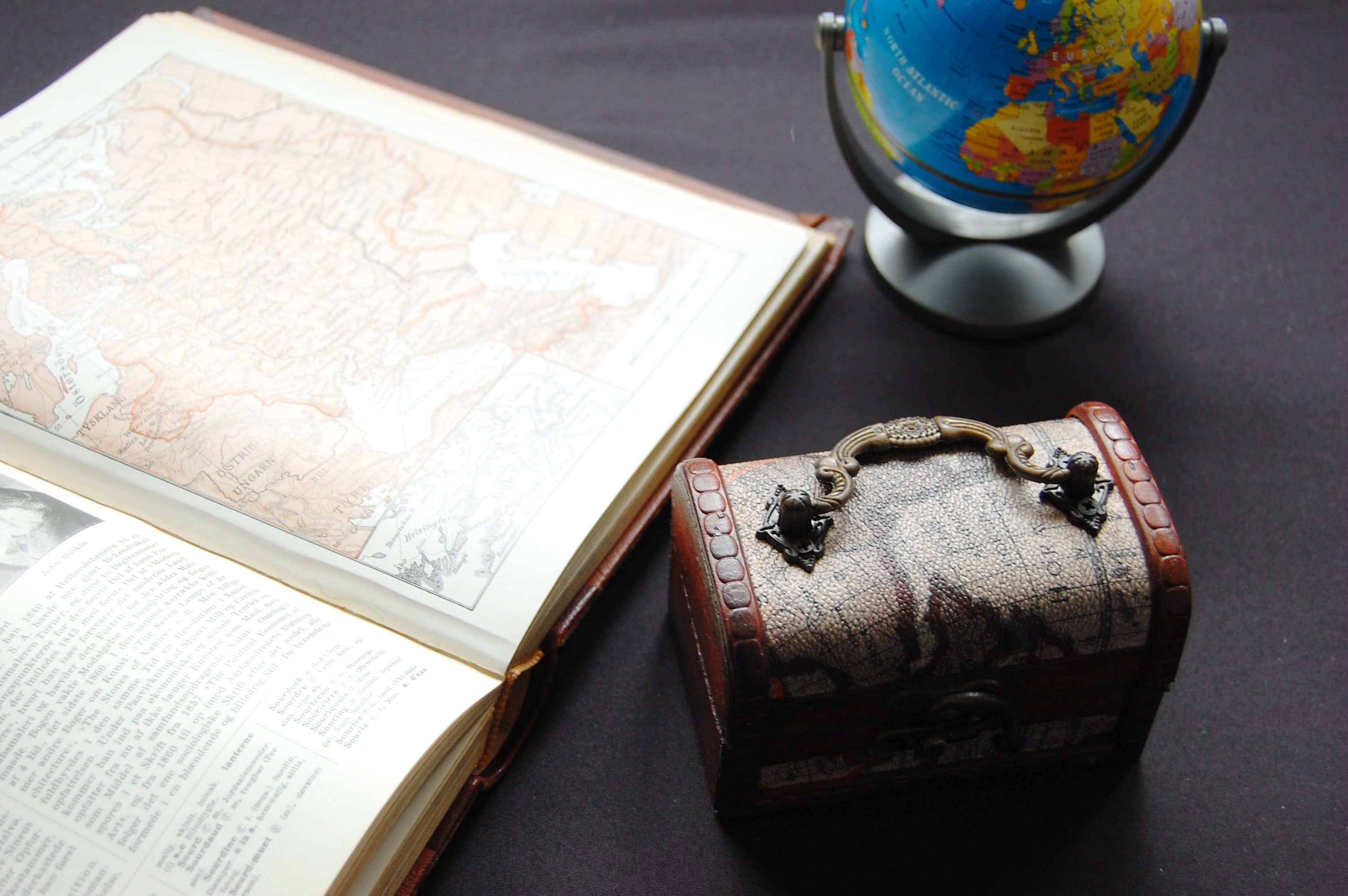 地図のページで開いた本と地球儀と鞄