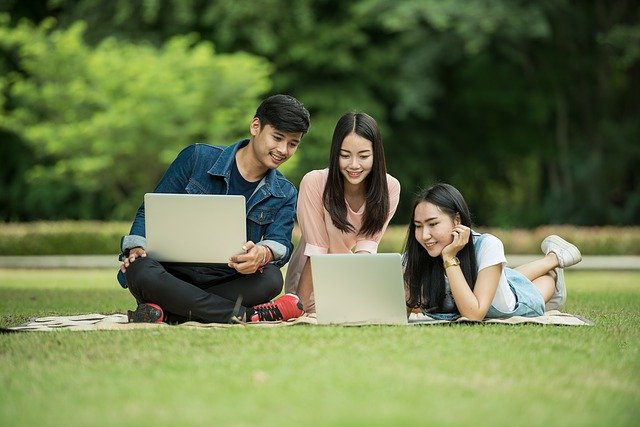 公園の芝生の上でくつろくアジア系の学生たち