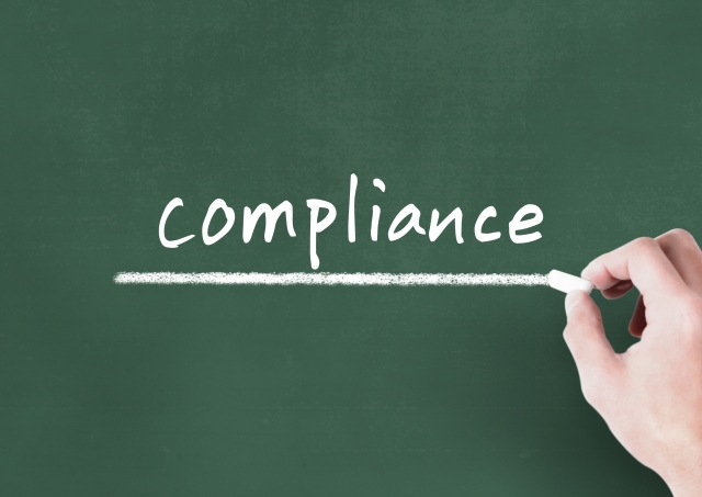 黒板にチョークで手書きされたcompliance(法令遵守)の文字