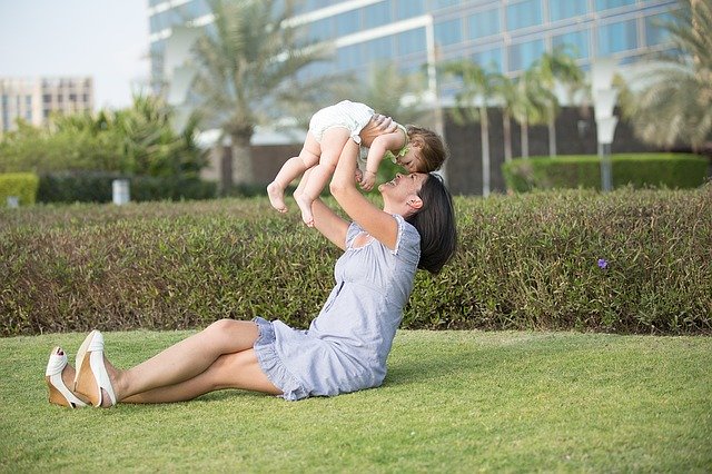 芝生の上に座り赤ん坊を抱き上げる母親