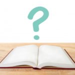 机の上に開かれた本とその上に浮かぶ緑色のクエスチョンマーク