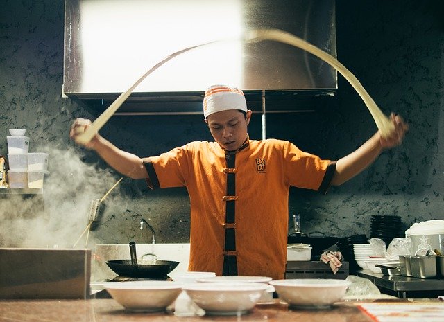 厨房にて真剣な表情で麺を打つ中華料理の調理師
