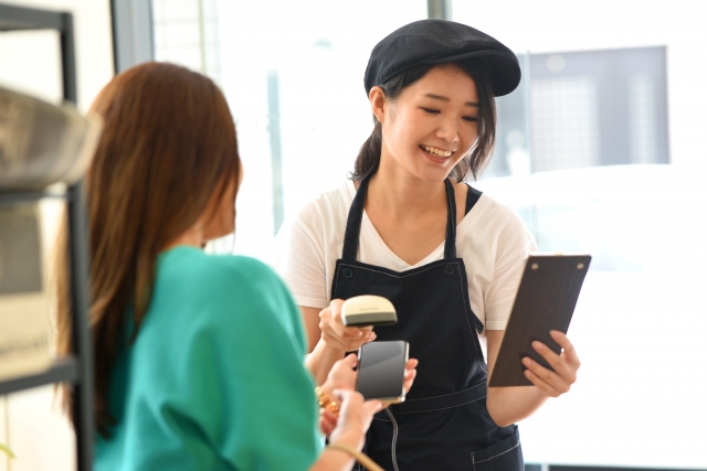 お客さんの支払いを処理する帽子を被った笑顔の店員女性