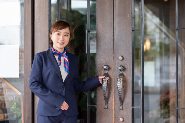 ホテルのエントランスで客のために扉を開ける準備をしている女性スタッフ