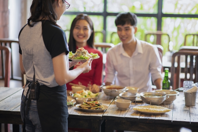 外国料理レストランで給仕するウェイトレスと笑顔のカップル客