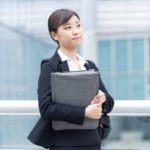 ファイルを抱えて歩くスーツ姿の若い女性