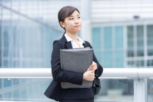 ファイルを抱えて歩くスーツ姿の若い女性
