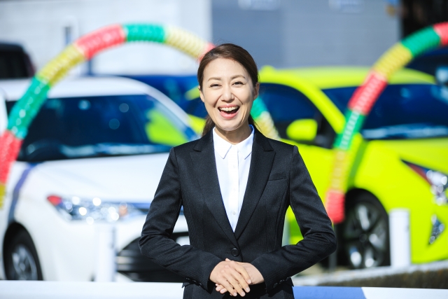 車販売店で笑顔で働くスーツ姿の女性販売員