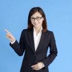 メガネをかけたスーツ姿の女性が指をさしている
