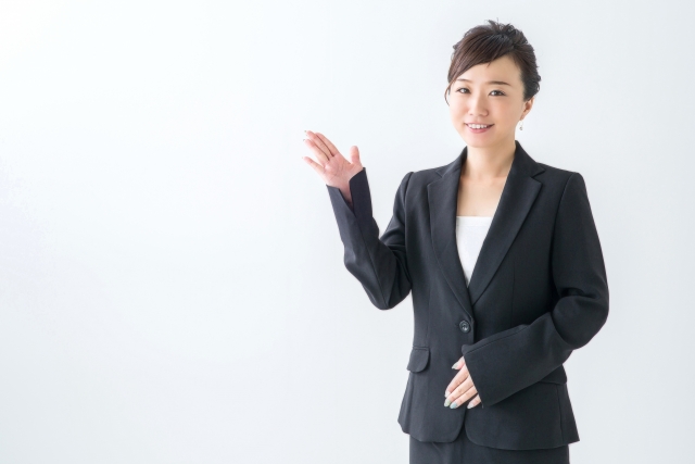 笑顔で何かを案内するスーツ姿の女性